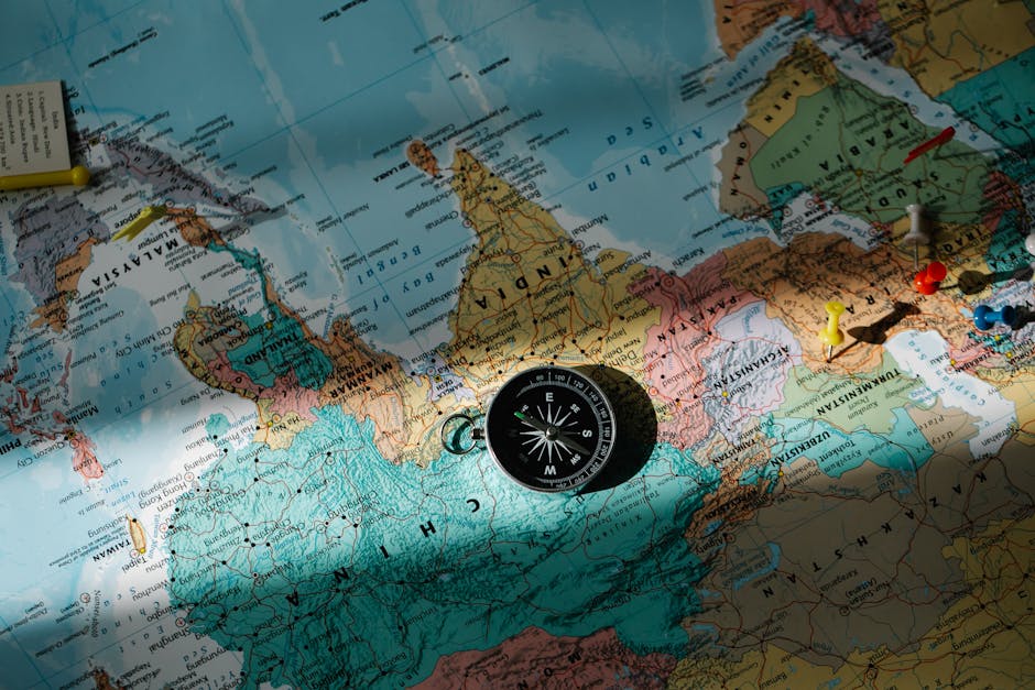 A compass placed on a detailed world map with colored push pins.